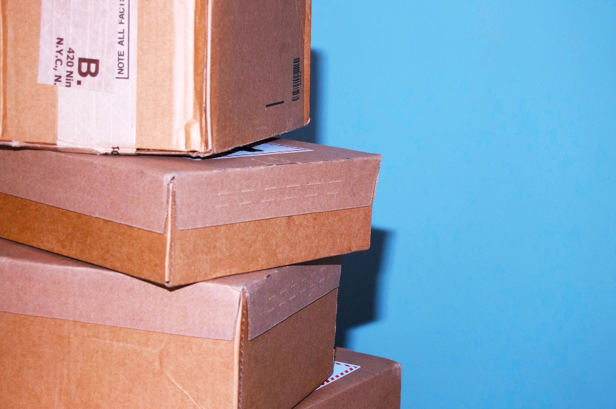 A few stacked cardboard delivery boxes for products against blue wall background.
