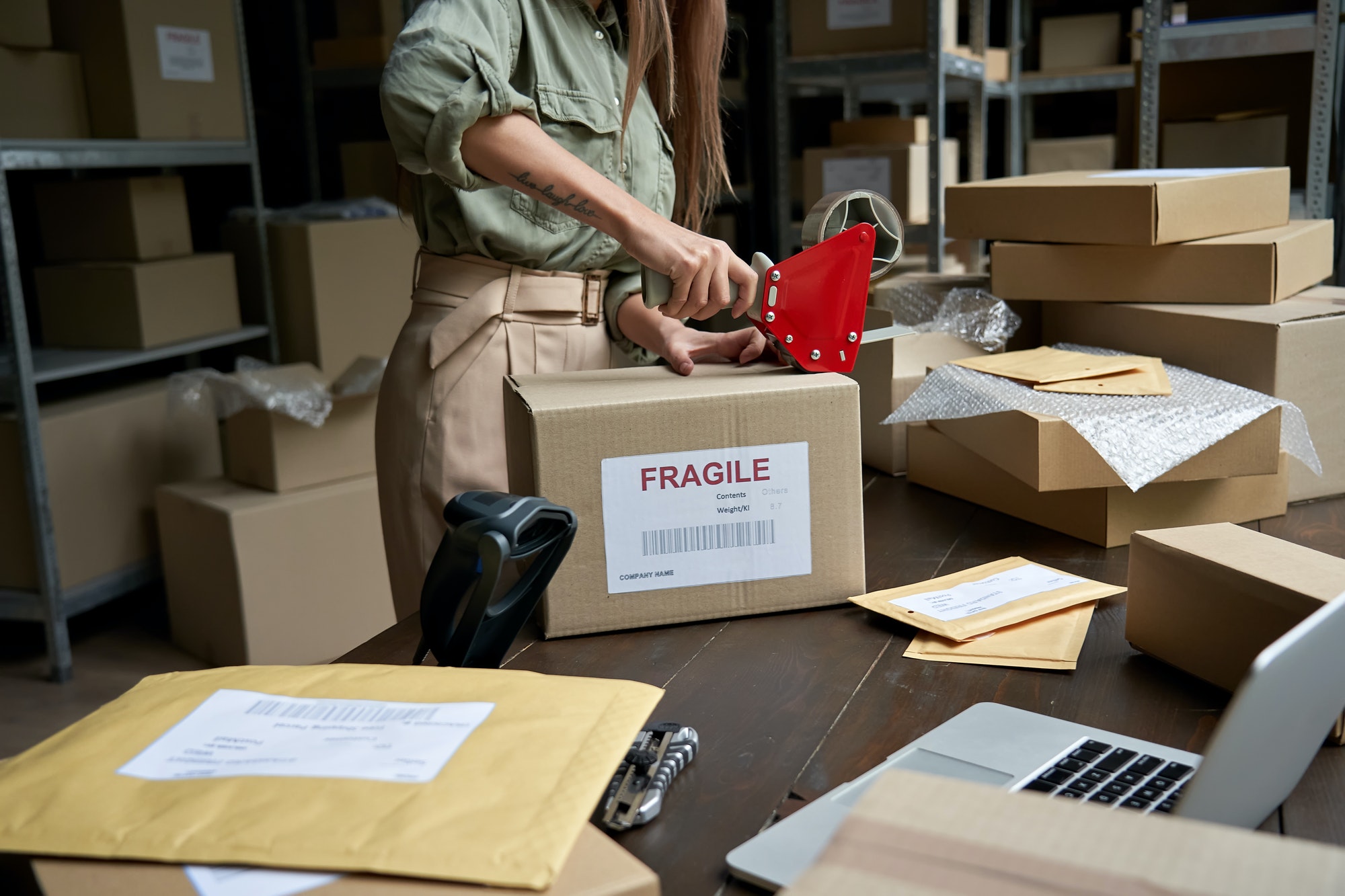Female post mail storage worker holding tape dispenser sealing shipping box.
